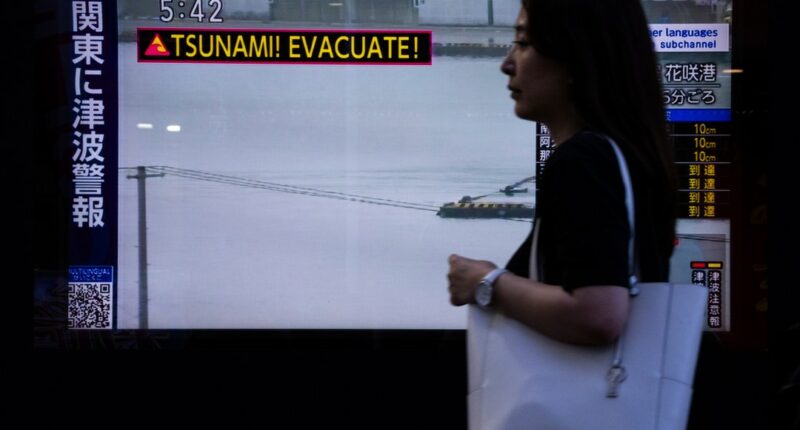 A pedestrian walks past a TV screen displaying a tsunami warning