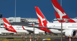 The vertical stabilisers of Qantas planes at Sydney Kingsford-Smith Airport, from the left: a Boeing B737-838 plane, registration VH-XZD; a Boeing B787-9 plane, registration VH-ZNE; and an Airbus A380-842 plane, registration VH-OQB. In the background on the left is a fourth Qantas plane, a Boeing B737-838, registration VH-XZH. In the far background is the international terminal.  In the foreground are navigational light structures at the northern end of the runway.  This image was taken from Nig