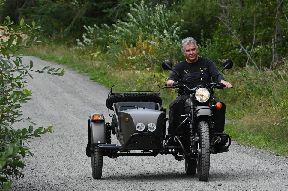 Man riding a Ural motorcycle with a sidecar on a gravel road.