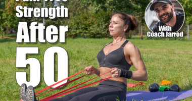 Muscular middle aged caucasian woman does seated row exercise for latissimus dorsi muscles using resistance band in city park on green grass. Black sportswear. Healthy lifestyle. Outdoor sport theme. 4 Pain-Free Exercises That Build Muscle Without Stress After 50, Say Experts. Cover