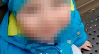 Photo of a toddler with their face blurred, wearing a blue jacket and hat.