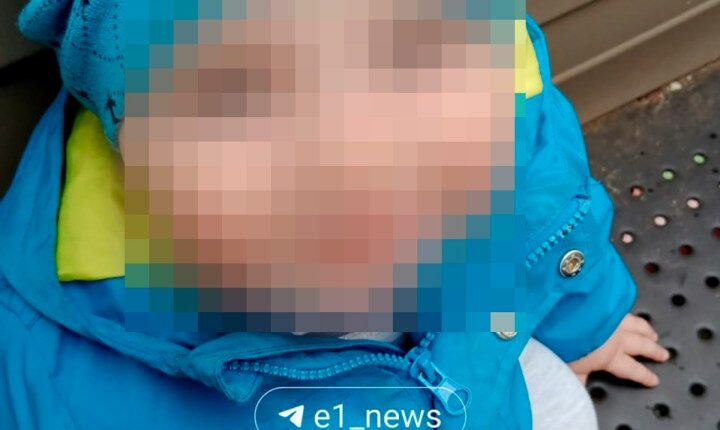 Photo of a toddler with their face blurred, wearing a blue jacket and hat.