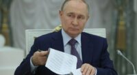 Vladimir Putin reviewing documents at a meeting.