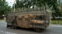 Military vehicle with cage armor driving down a road.