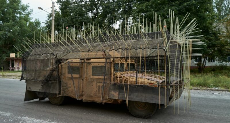 Military vehicle with cage armor driving down a road.