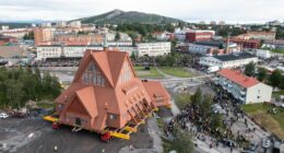 Aerial view of a church being moved on a transport system, with many people watching.