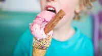Child eating strawberry ice cream cone with sprinkles and a chocolate bar.