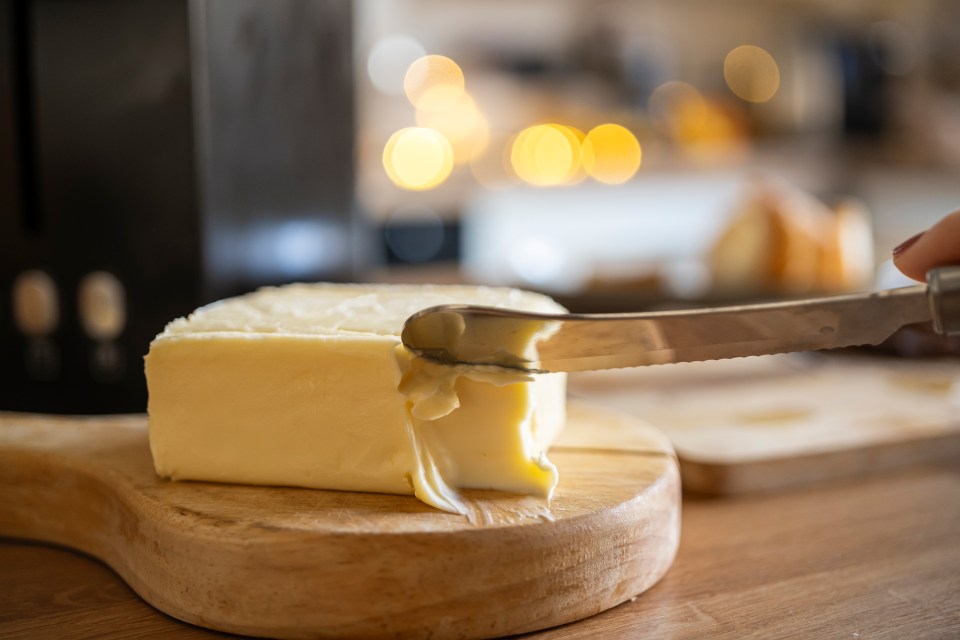 A knife cutting a block of butter on a wooden cutting board.