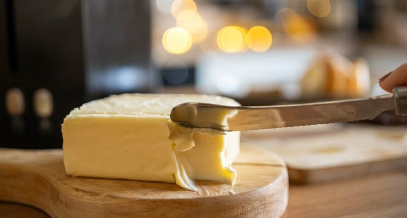 A knife cutting a block of butter on a wooden cutting board.