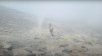 Two hikers walking on a foggy volcanic landscape.