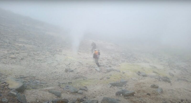 Two hikers walking on a foggy volcanic landscape.