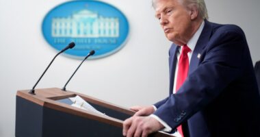 President Donald Trump at a podium listening to a reporter's question.