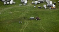 Aerial view of a tractor spreading manure on a field with several caravans parked nearby.