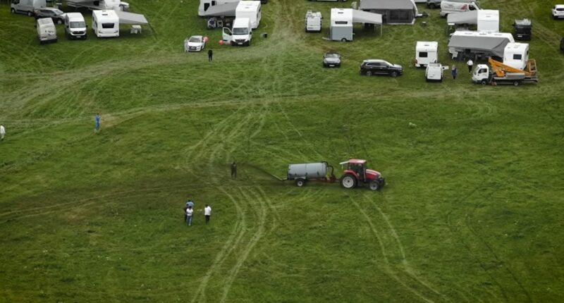 Aerial view of a tractor spreading manure on a field with several caravans parked nearby.