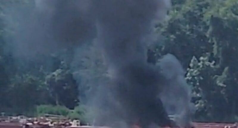 Smoke rising from a barge fire on a river.