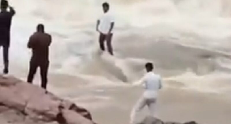 People watching a man standing in turbulent water.