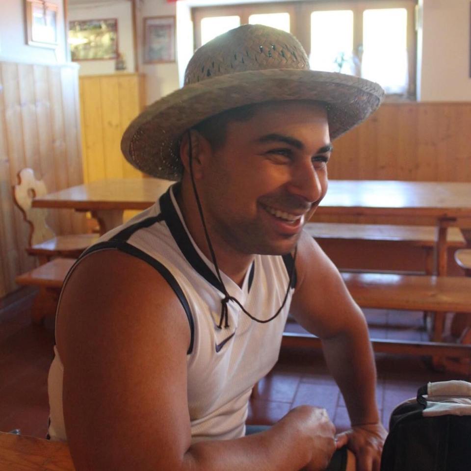 Man smiling while wearing a straw hat and sleeveless shirt.