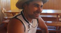 Man smiling while wearing a straw hat and sleeveless shirt.