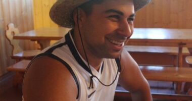 Man smiling while wearing a straw hat and sleeveless shirt.