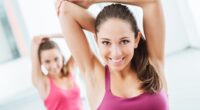 Young women at the gym sitting on a mat and doing stretching exercises for arms