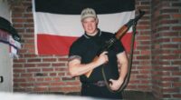 Photo of a young man holding a rifle, standing in front of a German flag.