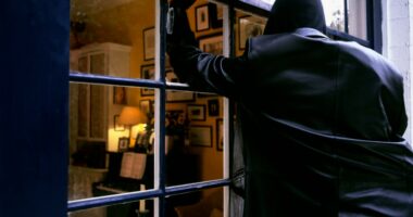 A burglar breaking into a house through a window.