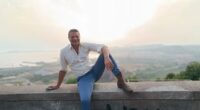 Luigi Di Sarno, 52, sitting on a wall overlooking a city.