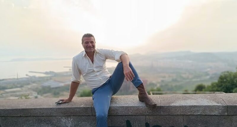 Luigi Di Sarno, 52, sitting on a wall overlooking a city.