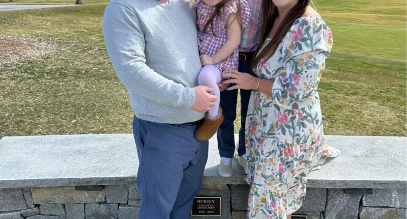 Family photo of four people in front of a stone wall.