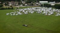 Aerial view of a tractor spreading manure near numerous RVs parked in a field.