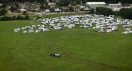 Aerial view of a tractor spreading manure near numerous RVs parked in a field.