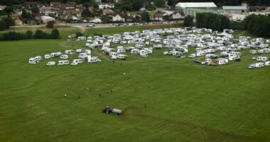 Aerial view of a tractor spreading manure near numerous RVs parked in a field.