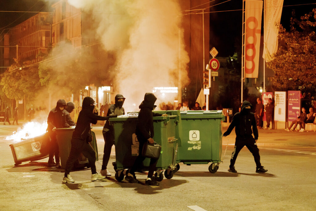 People carry containers to the middle of the street and set them on fire to create barricades in Lausanne, Switzerland