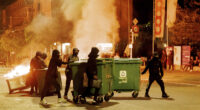 People carry containers to the middle of the street and set them on fire to create barricades in Lausanne, Switzerland