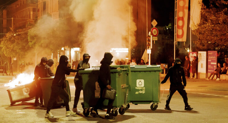 People carry containers to the middle of the street and set them on fire to create barricades in Lausanne, Switzerland