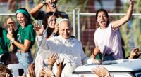 Pope Leo XIV waving from a popemobile to young people at a Jubilee of Youth Mass.