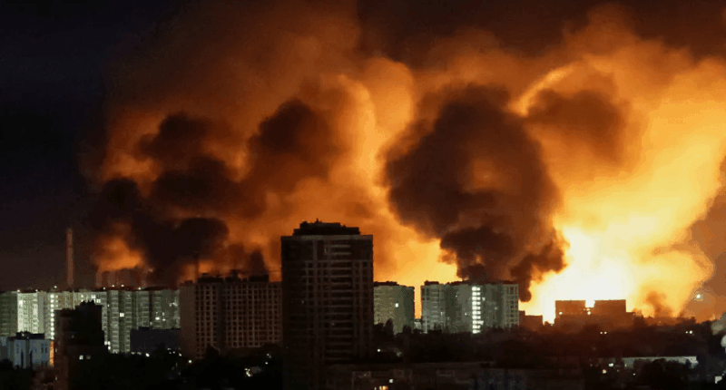 Large fire behind city buildings at night.