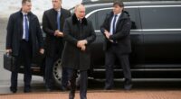 Vladimir Putin with bodyguards near a car.