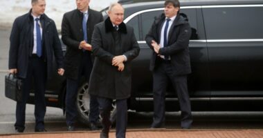 Vladimir Putin with bodyguards near a car.