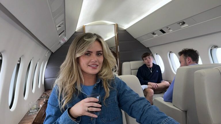 Woman seated in a private jet with two men in the background.