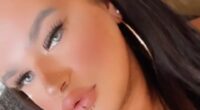 Close-up selfie of a person with long dark hair, wearing hoop earrings and lip piercing.