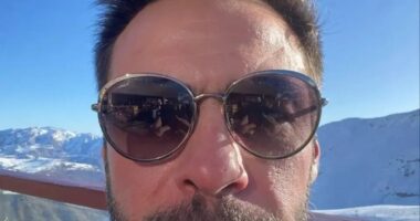 Selfie of a man wearing sunglasses, with snowy mountains in the background.