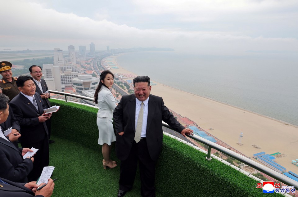 Kim Jong Un and his daughter overlooking a beach from a balcony.