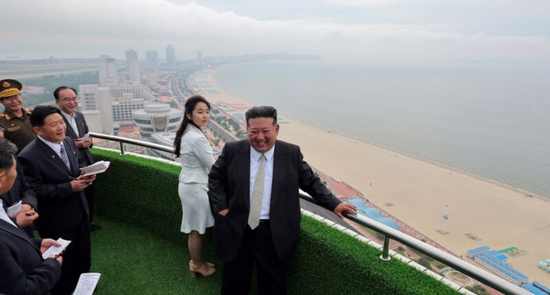 Kim Jong Un and his daughter overlooking a beach from a balcony.