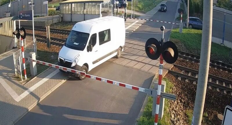 A white van narrowly avoids being hit by a train at a railway crossing.