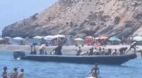 A boat arrives at a beach carrying a large group of people.