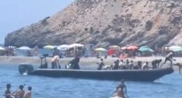 A boat arrives at a beach carrying a large group of people.