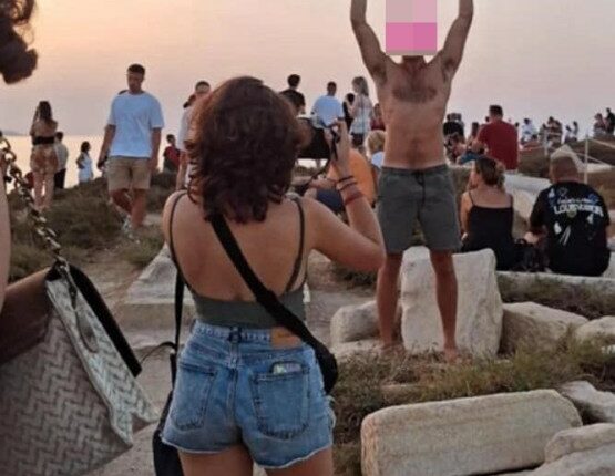 Tourist lifting ancient stone block at sunset.