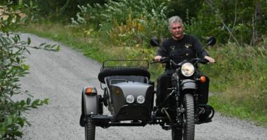 Man riding a Ural motorcycle with a sidecar on a gravel road.