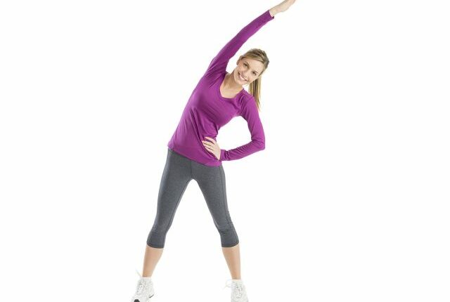 Full length portrait of happy young woman with arms raised doing stretching exercise against white background